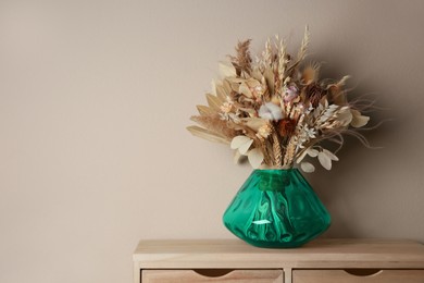 Beautiful dried flower bouquet in glass vase on wooden table near light grey wall. Space for text