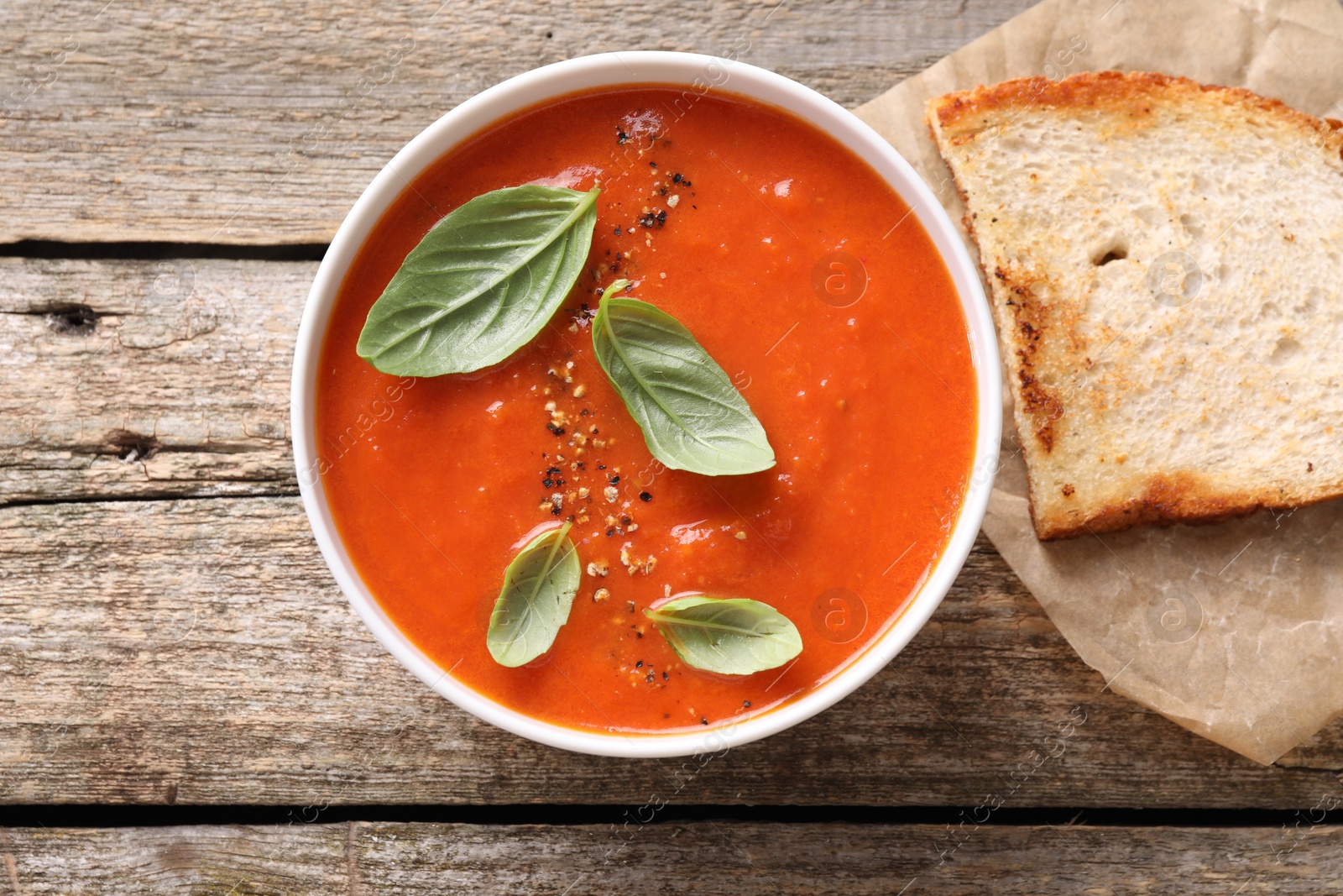 Photo of Delicious tomato soup with basil, spices and bread on wooden table, flat lay