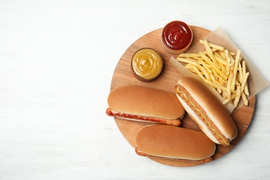 Photo of Composition with hot dogs, french fries and sauce on wooden table, top view. Space for text