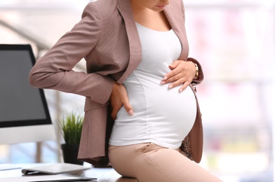 Young pregnant woman in suit at workplace, closeup