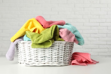 Photo of Wicker basket with towels on table near white brick wall
