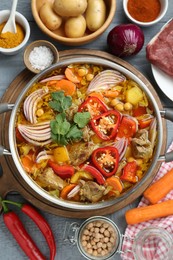 Photo of Delicious vegetable soup with meat in saucepan and ingredients on grey wooden table, flat lay