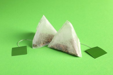 Photo of New tea bags with tabs on green background, closeup