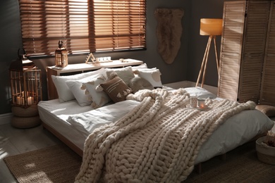Photo of Cozy bedroom interior with knitted blanket and cushions