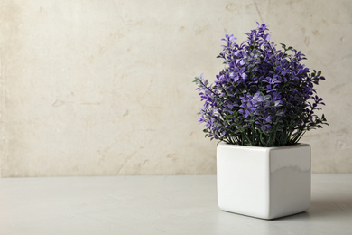Photo of Purple artificial plant in white flower pot on table against light background. Space for text