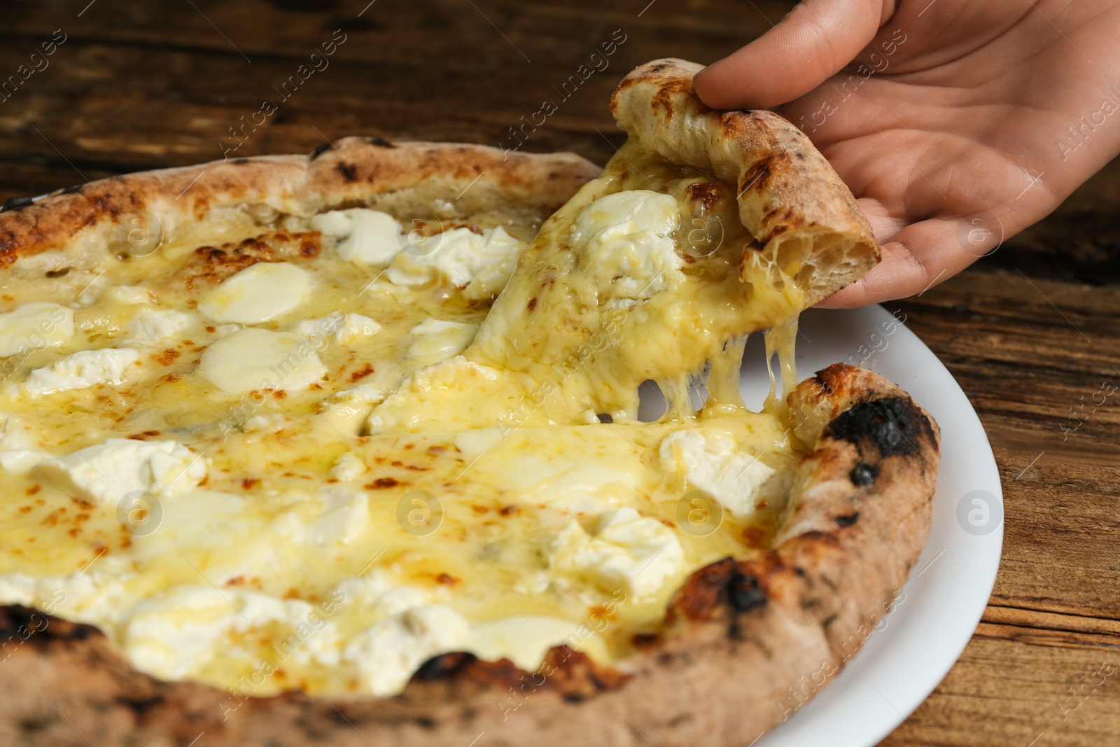 Photo of Woman taking slice of tasty cheese pizza at wooden table, closeup