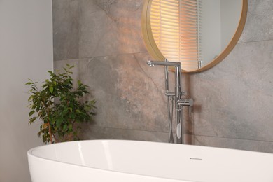 Photo of Spa day. Stylish bathroom interior with ceramic tub, mirror and green houseplant