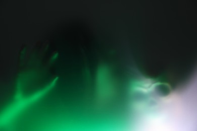 Photo of Silhouette of creepy ghost with skull behind glass against color background