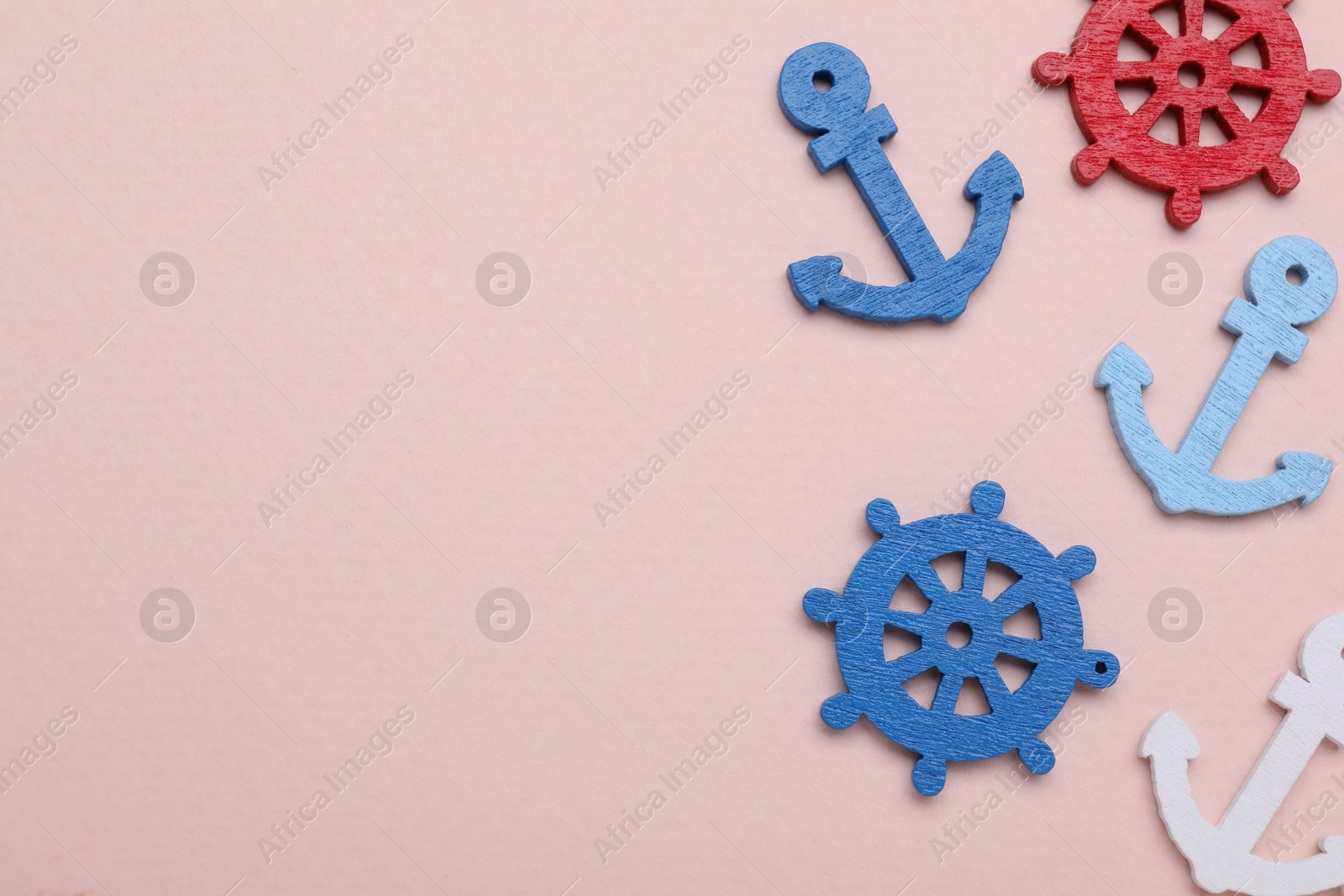 Photo of Anchor and ship wheel figures on pale pink background, flat lay. Space for text