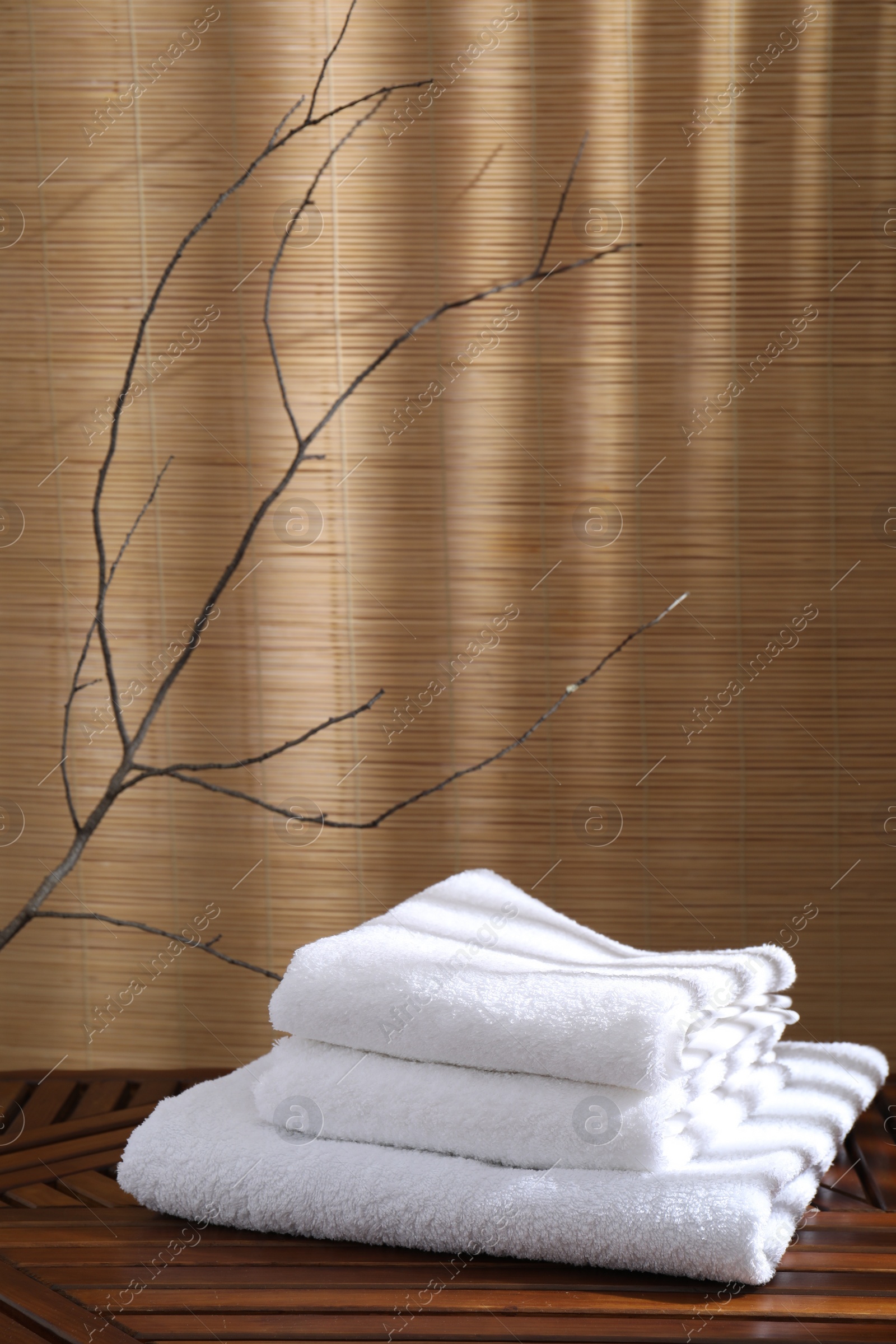 Photo of Stacked soft towels on wooden table and tree branches indoors