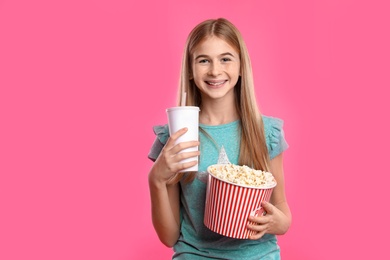 Teenage girl with popcorn and beverage during cinema show on color background