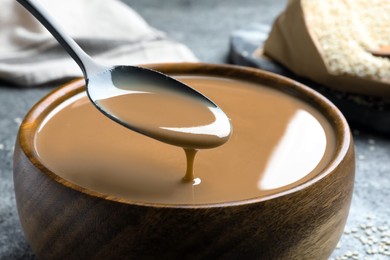 Photo of Spoon of tasty sesame paste above bowl, closeup