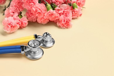 Photo of Stethoscopes and beautiful flowers on beige background, space for text. Happy Doctor's Day