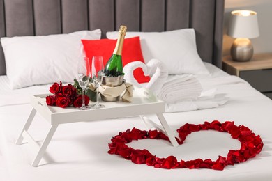 Photo of Honeymoon. Swans made with towels, heart of beautiful rose petals and sparkling wine on bed in room