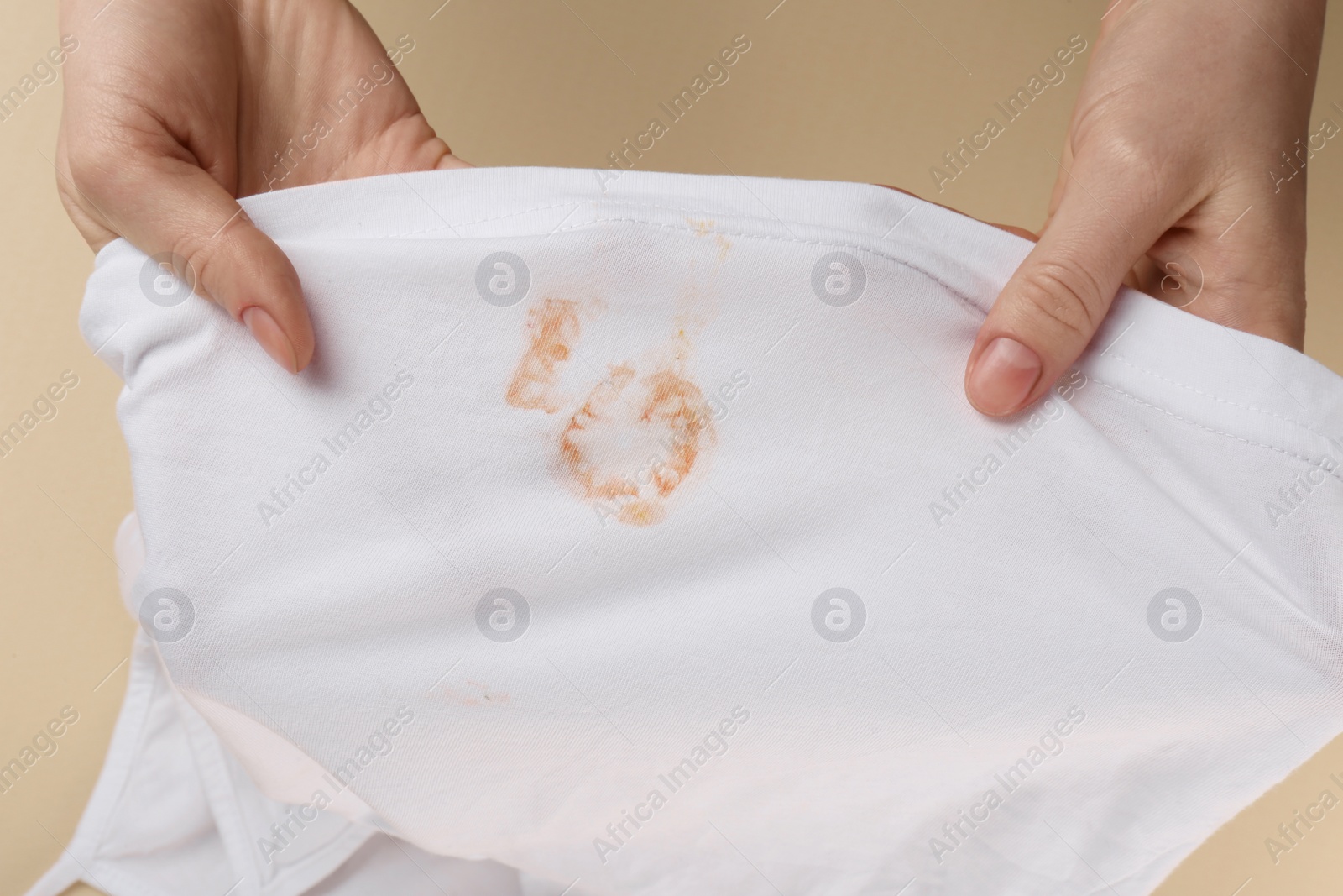 Photo of Woman holding white shirt with yellow stains on beige background, top view