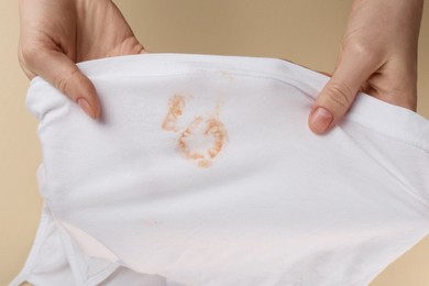 Woman holding white shirt with yellow stains on beige background, top view