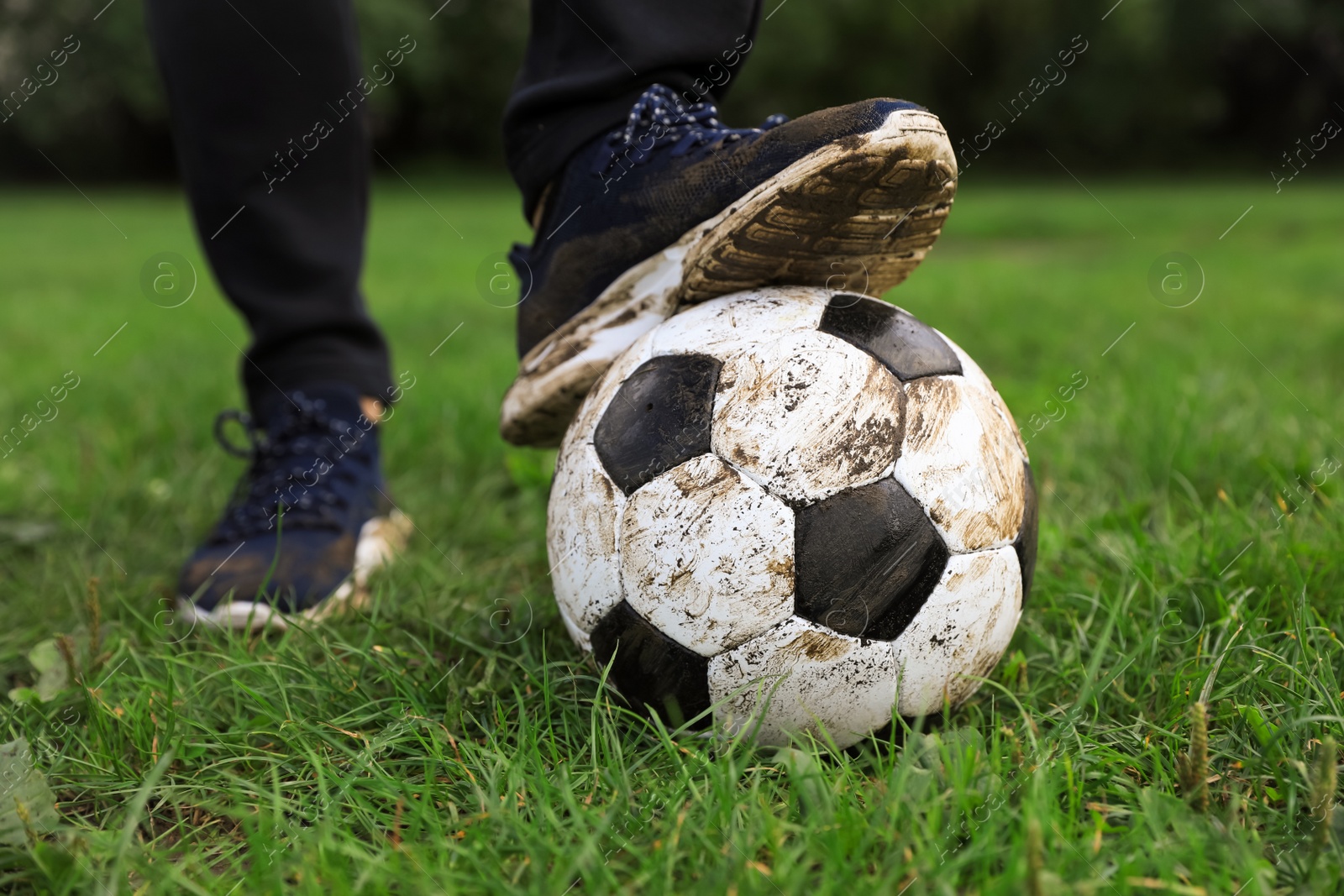 Photo of Man with dirty soccer ball on green grass outdoors, closeup