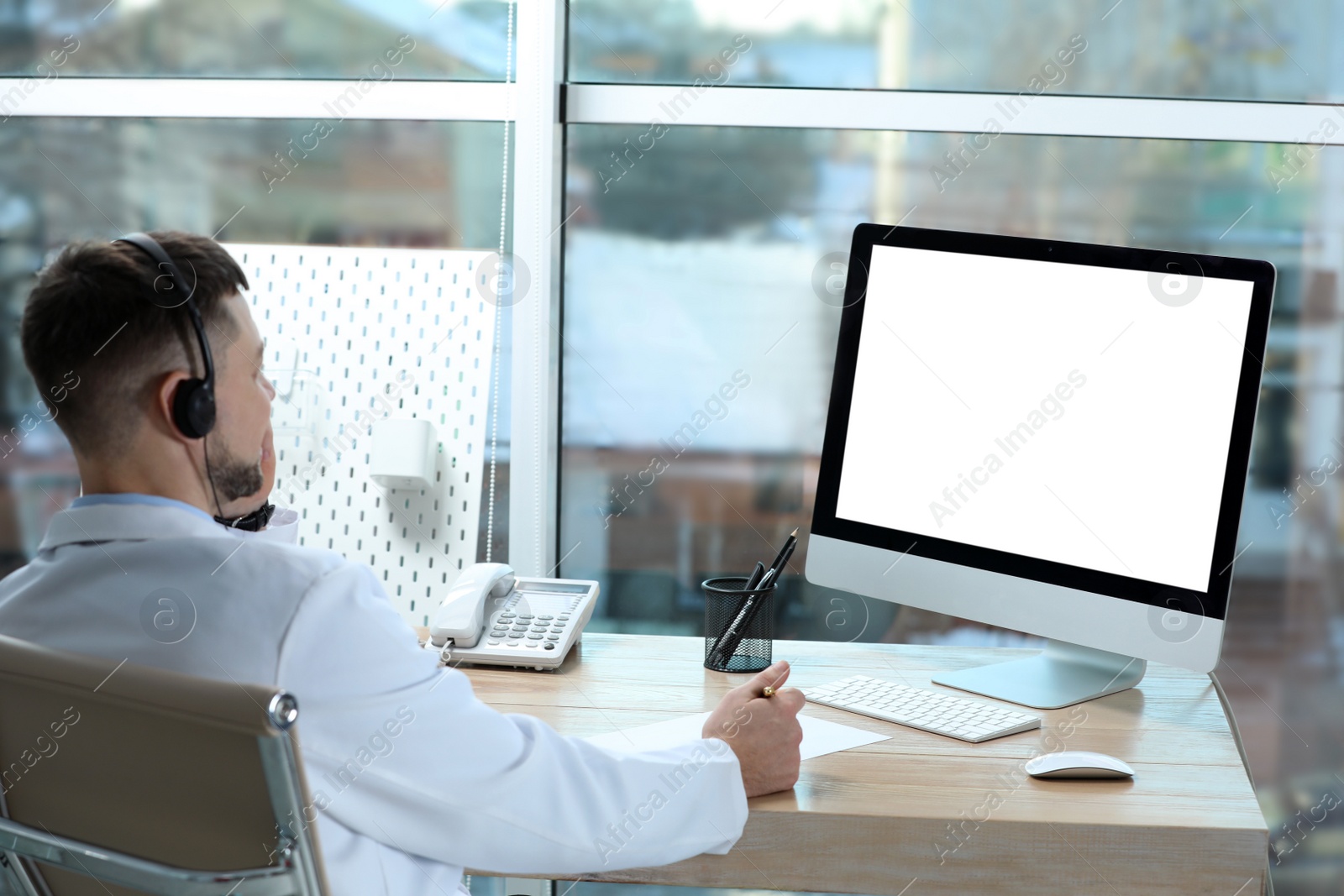 Photo of Doctor with headset consulting patient online at desk in clinic, space for text. Health service hotline