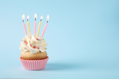 Photo of Birthday cupcake with candles on light blue background. Space for text