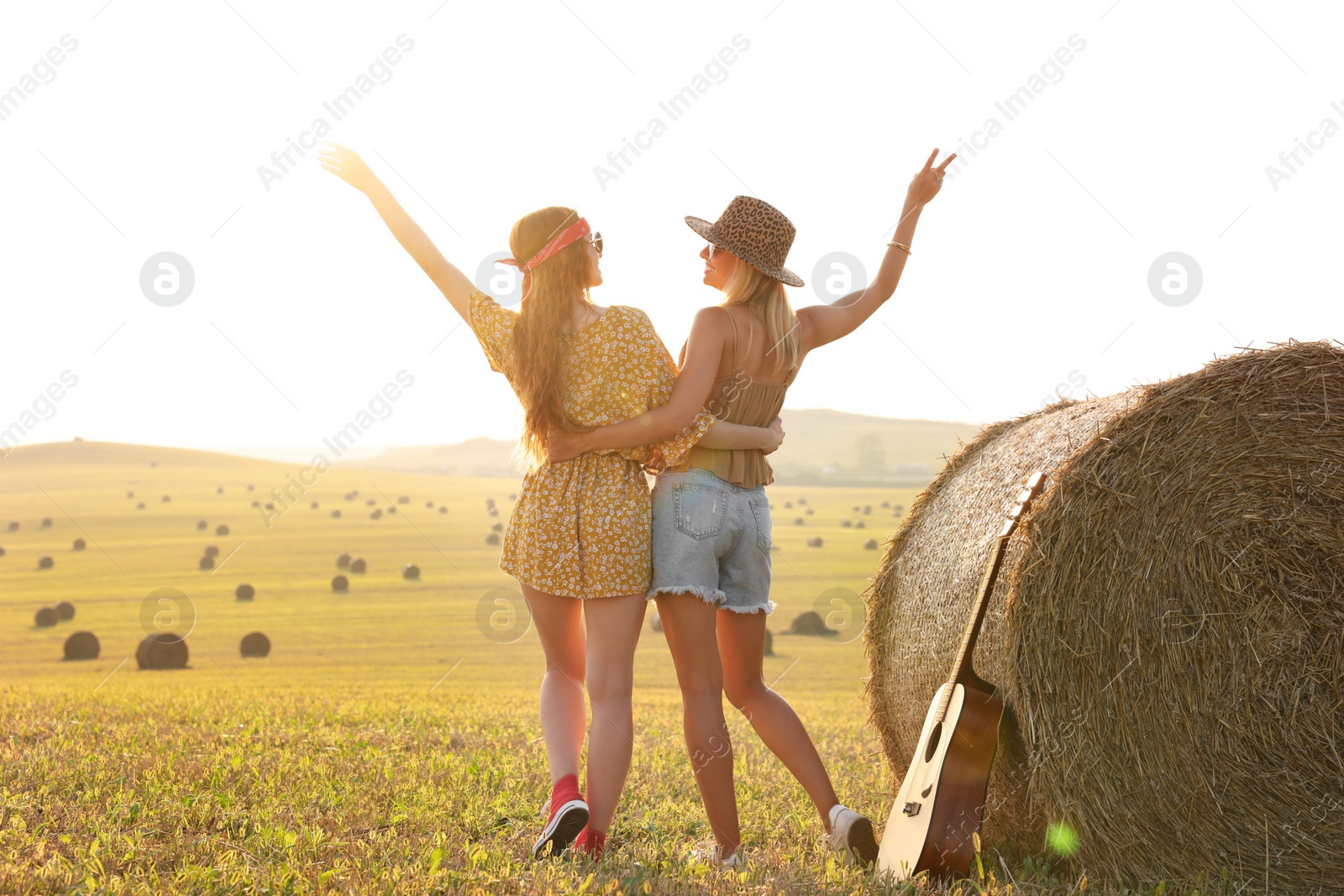 Photo of Happy hippie women near hay bale in field, back view