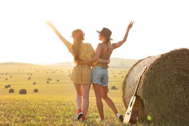 Happy hippie women near hay bale in field, back view