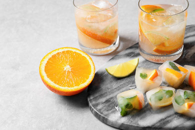 Photo of Ice cubes with orange and mint on light grey table