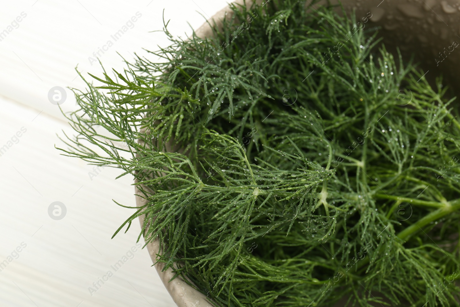 Photo of Bowl of fresh green dill with water drops on white wooden table, above view