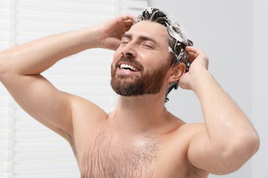 Happy man washing his hair with shampoo in shower