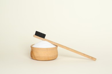 Bamboo toothbrush and bowl with baking soda on beige background
