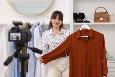 Photo of Smiling fashion blogger showing her clothes while recording video at home