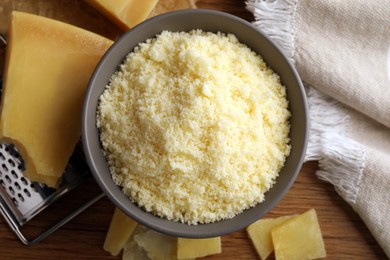 Photo of Delicious grated parmesan cheese in bowl on wooden table, flat lay