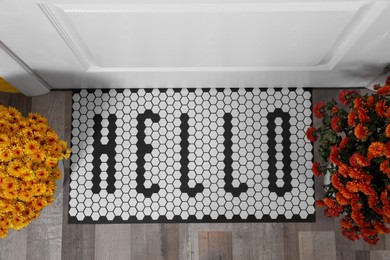 Photo of Stylish door mat with word Hello and beautiful flowers, flat lay