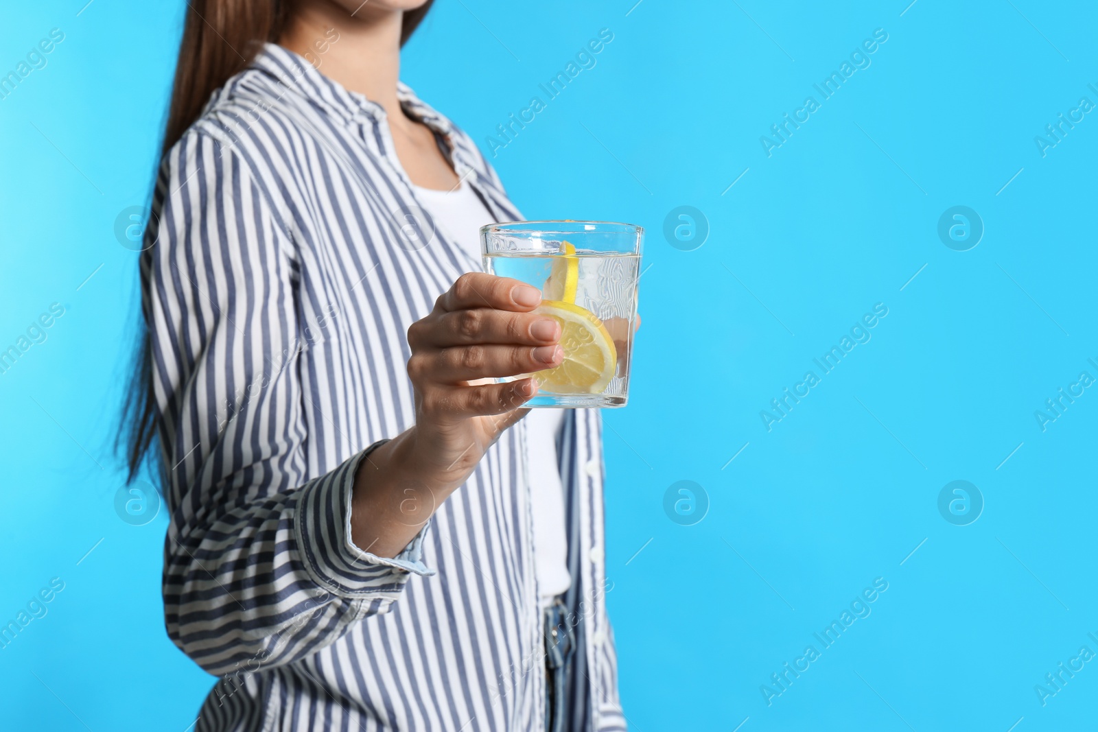 Photo of Young woman with glass of lemon water on light blue background, closeup