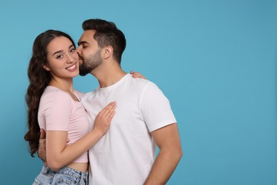 Man kissing his smiling girlfriend on light blue background. Space for text