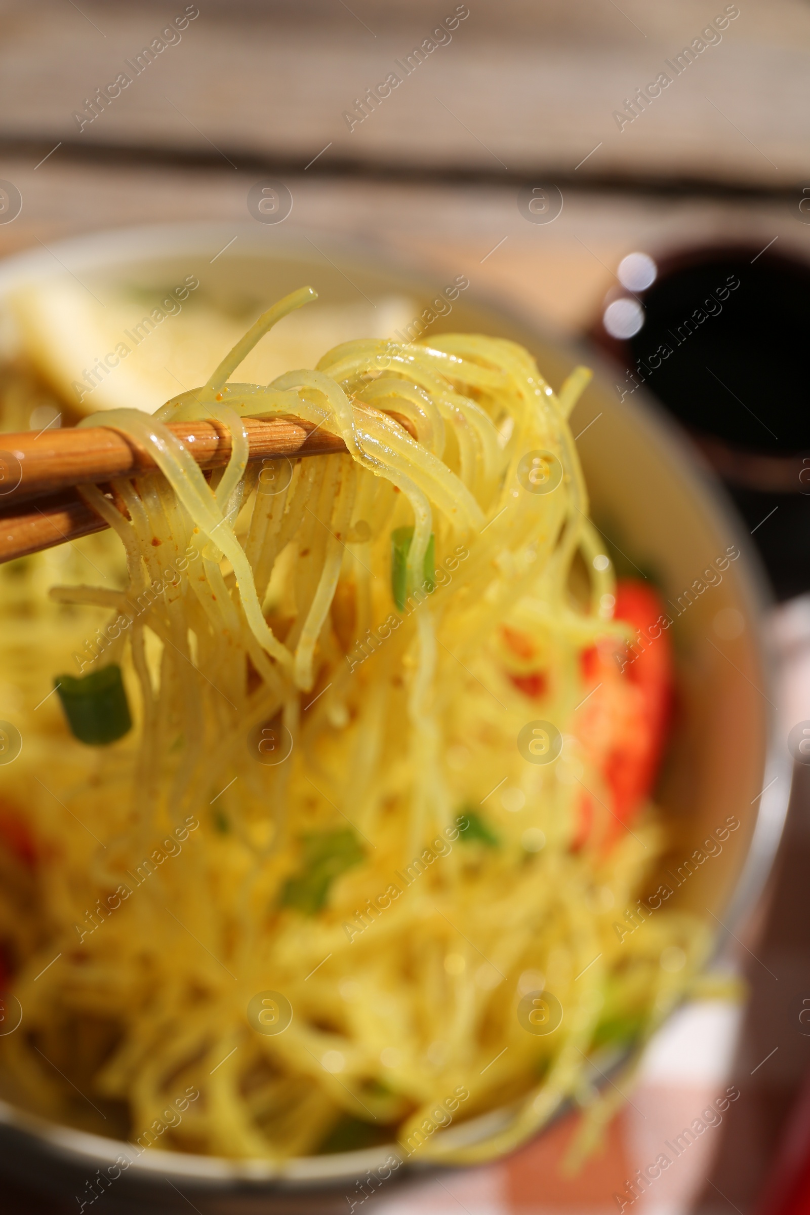 Photo of Stir-fry. Eating tasty noodles with chopsticks at table, closeup