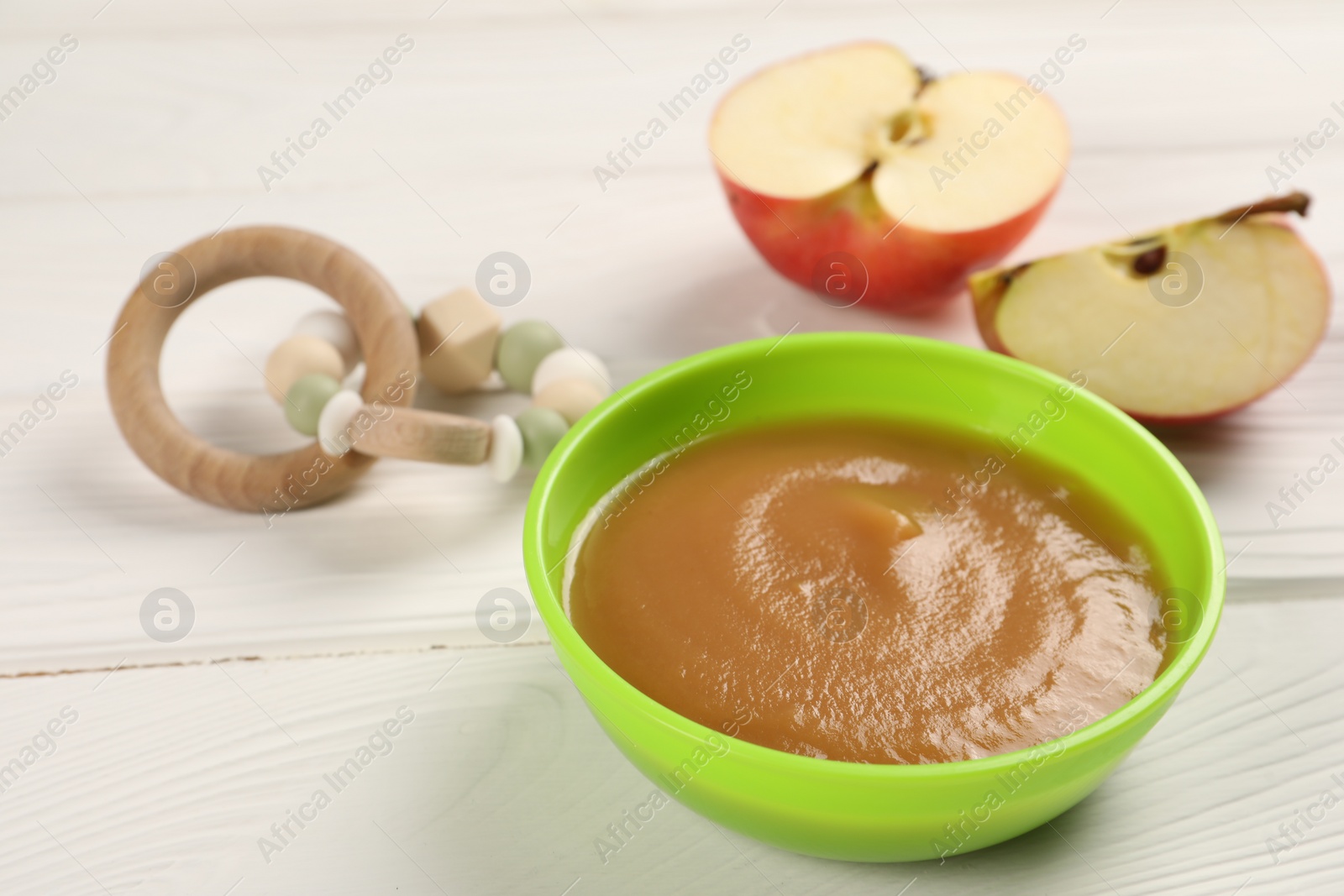 Photo of Baby food. Puree of apples in bowl and toy on white wooden table