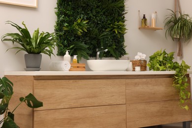 Photo of Green artificial plants, vanity and different personal care products in bathroom