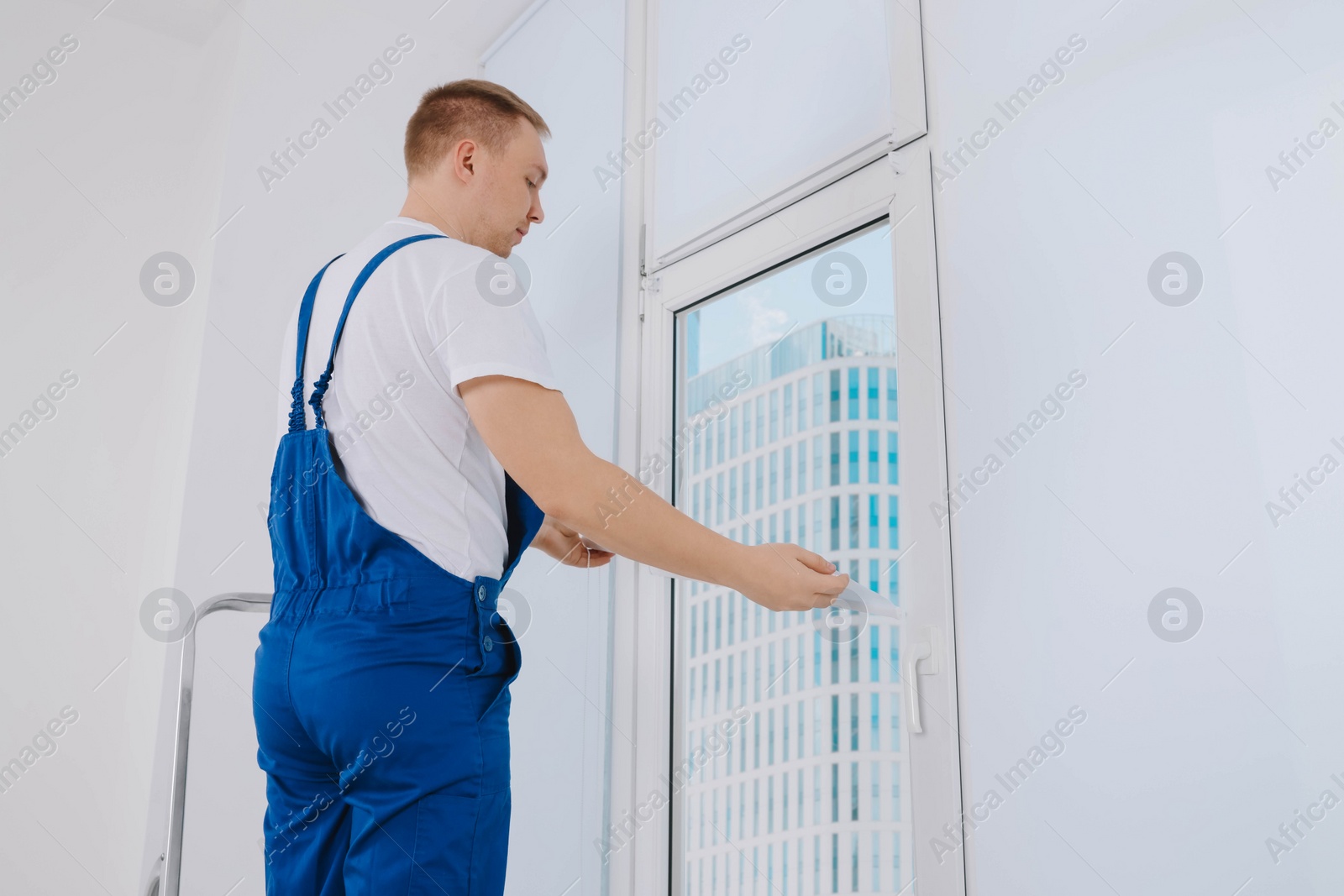 Photo of Worker installing roller window blind on stepladder indoors