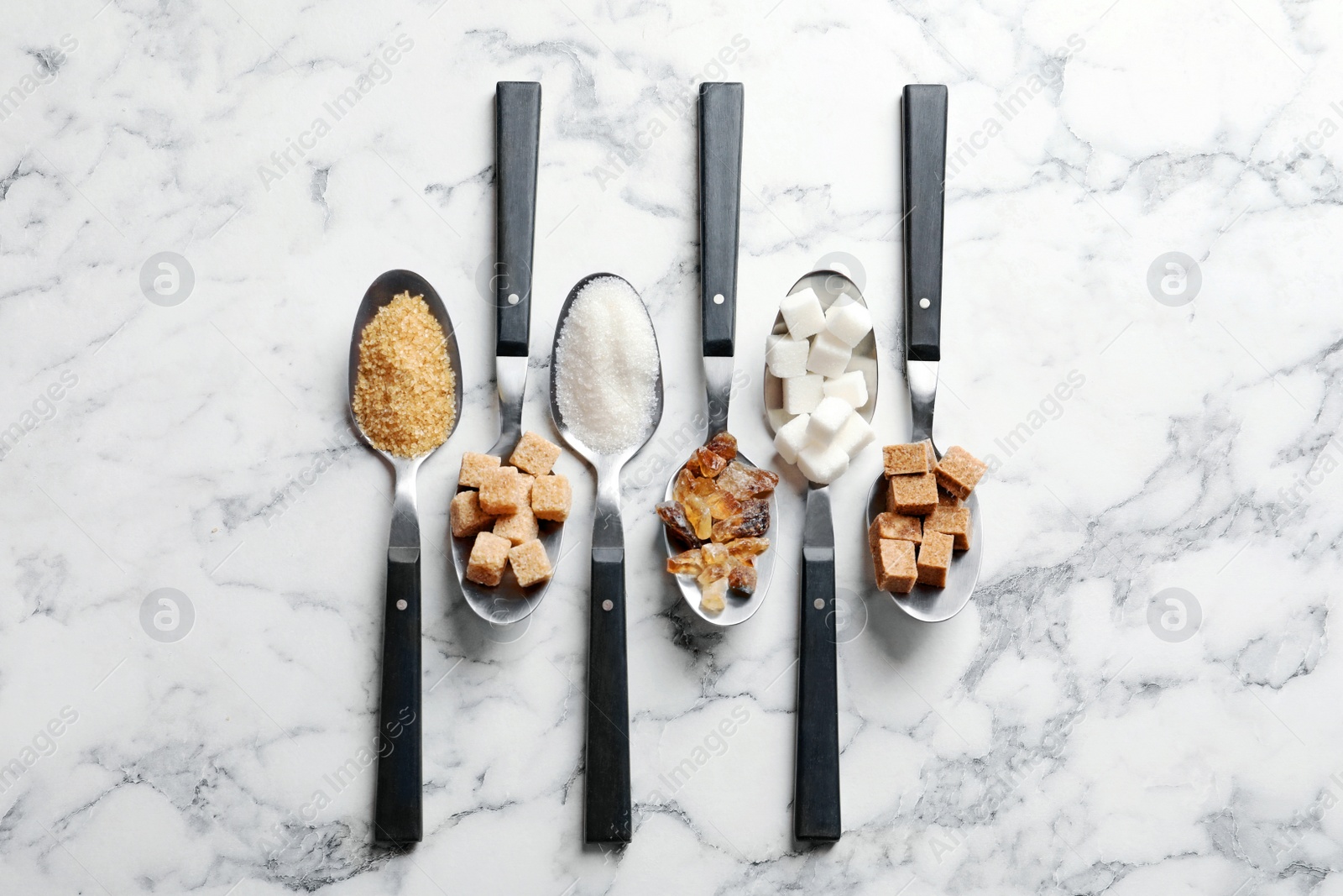 Photo of Spoons with different types of sugar on marble background