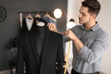 Young tailor taking measurements of jacket on mannequin in atelier