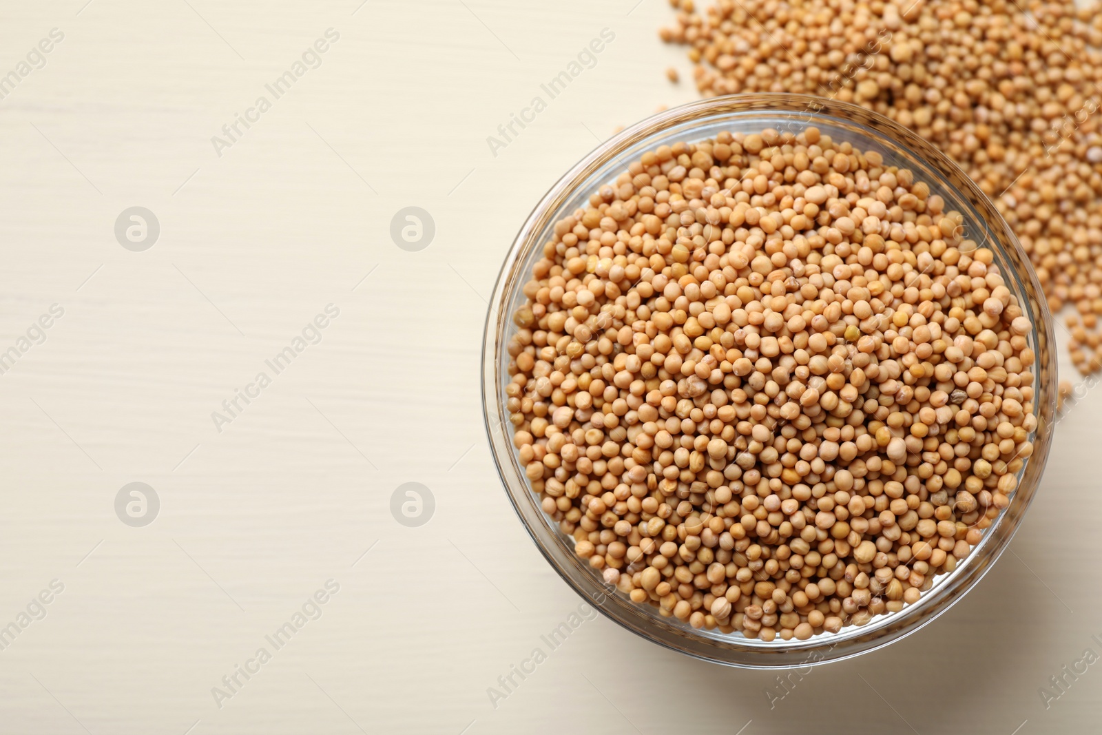 Photo of Mustard seeds with bowl on white wooden table, top view. Space for text