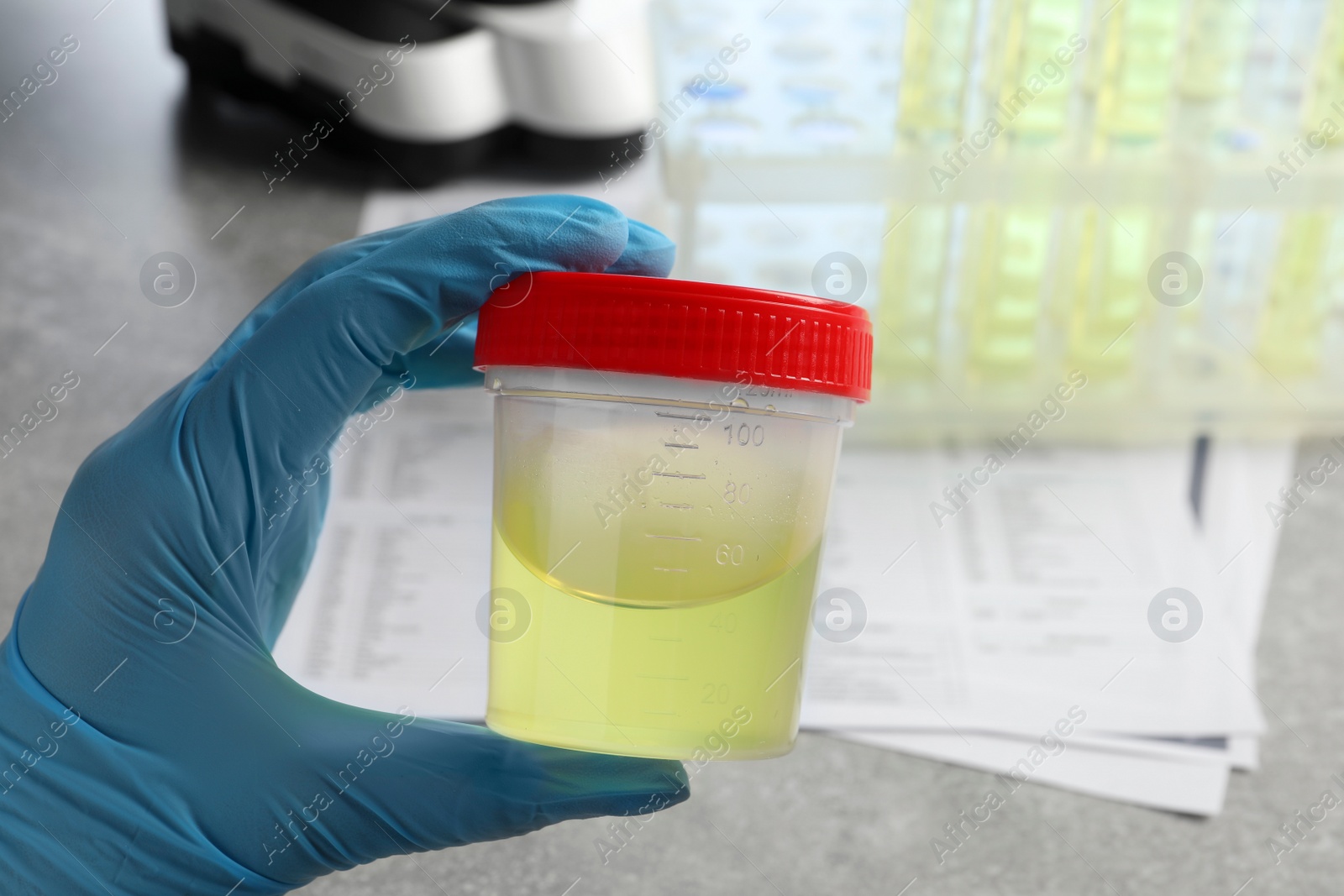 Photo of Doctor holding container with urine sample for analysis at grey table in laboratory, closeup