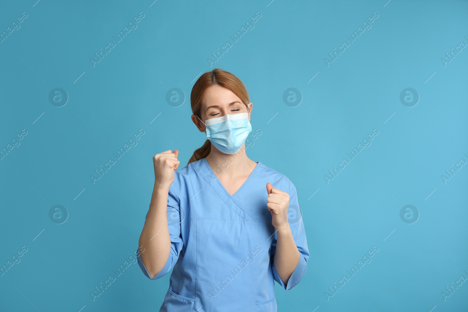 Photo of Emotional doctor with protective mask on light blue background. Strong immunity concept