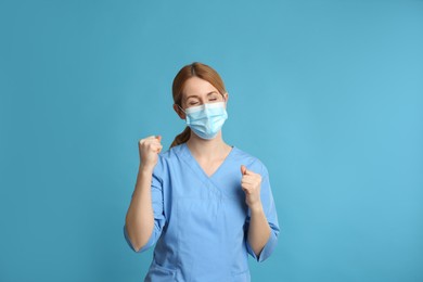 Photo of Emotional doctor with protective mask on light blue background. Strong immunity concept