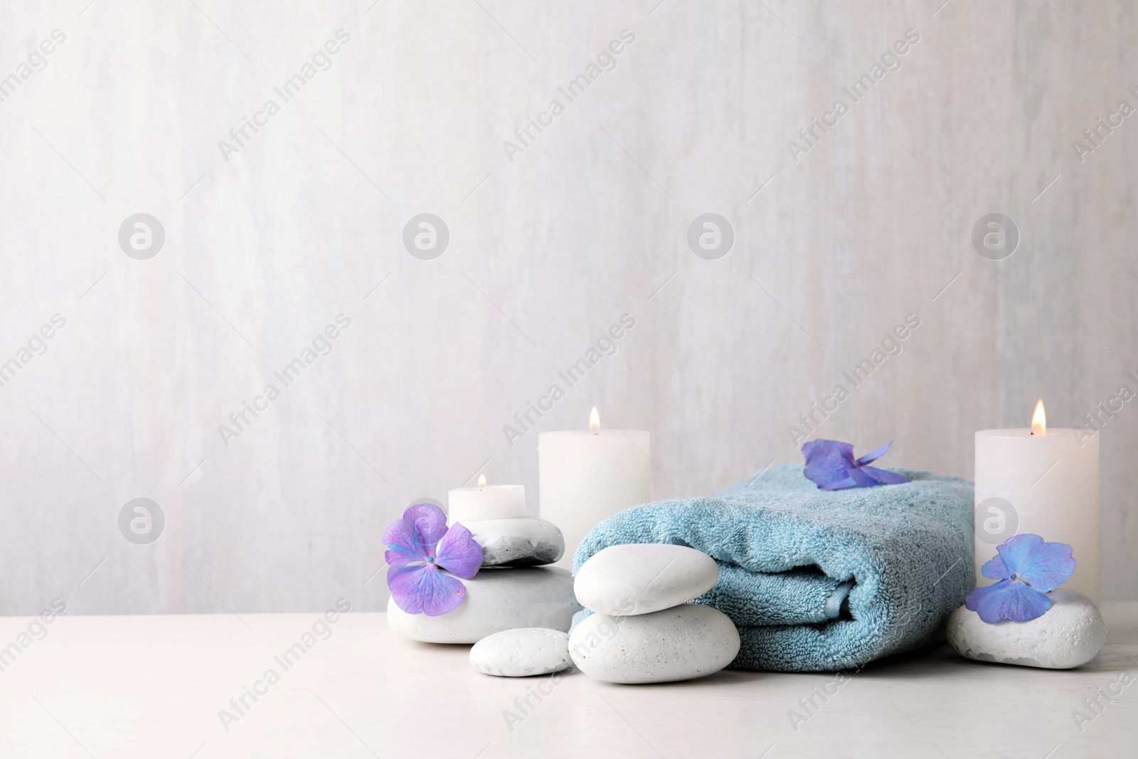 Photo of Composition with zen stones, towel and candles on table against light background. Space for text