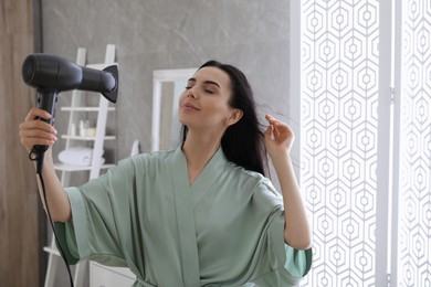 Photo of Beautiful young woman using hair dryer in bathroom