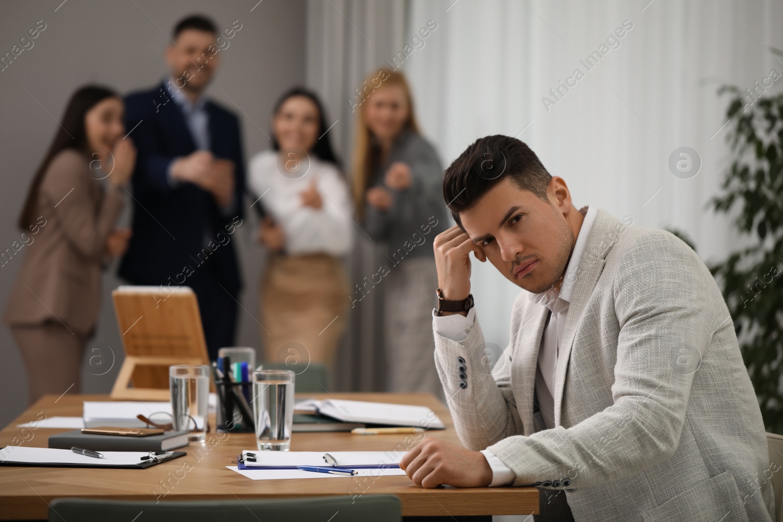 Photo of Coworkers bullying their colleague at workplace in office, space for text