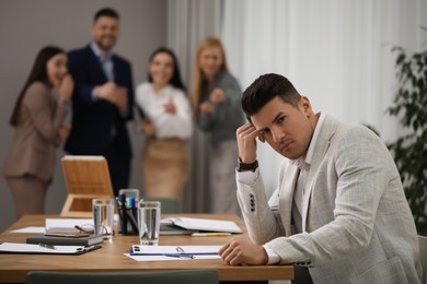 Photo of Coworkers bullying their colleague at workplace in office, space for text