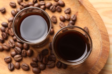 Photo of Shot glasses with coffee liqueur and beans on wooden table, top view