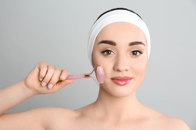 Photo of Woman using natural pink quartz face roller on grey background